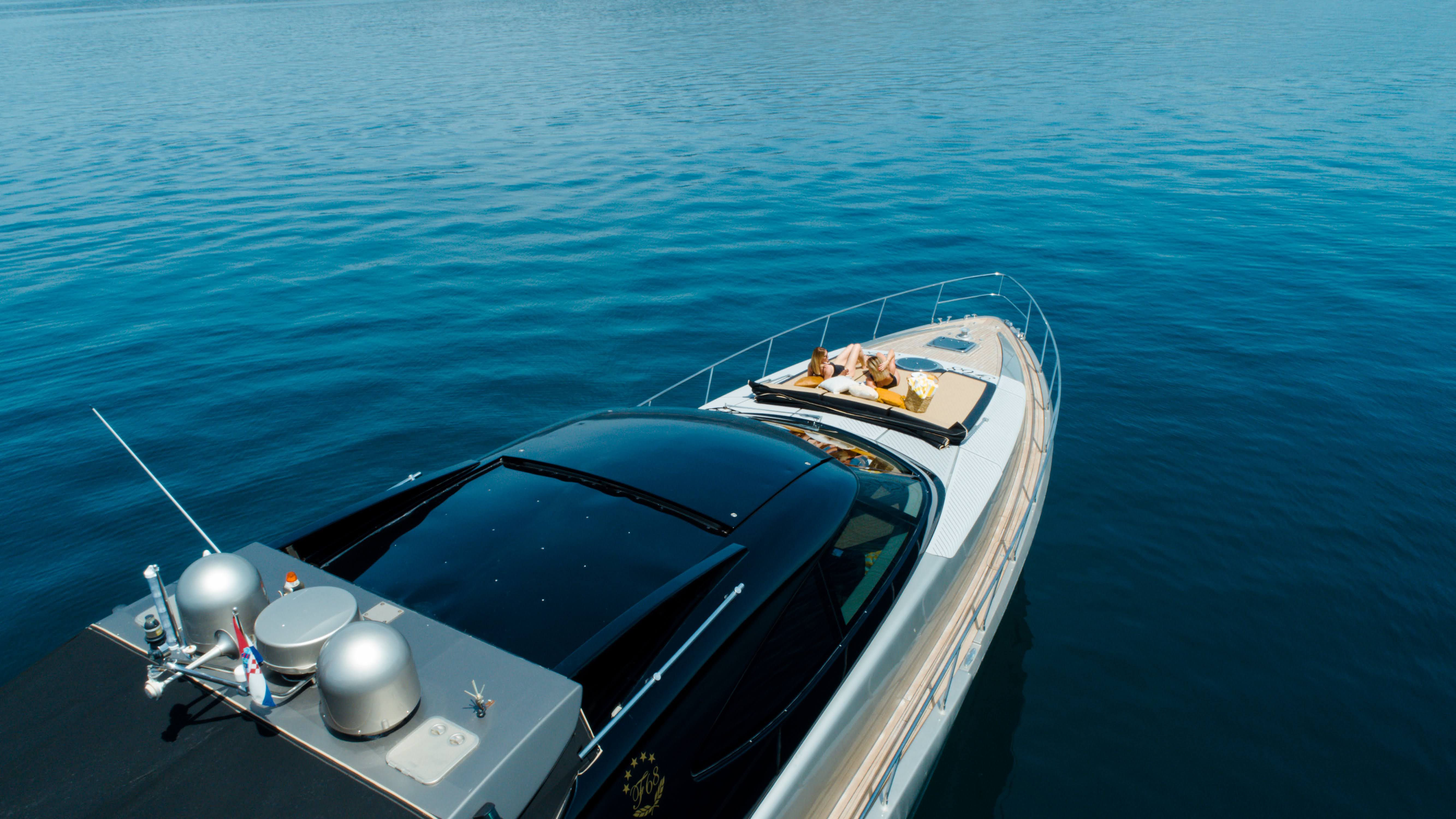 Aerial view of Luxury F68 motor yacht with sunbathers on the deck floating on calm blue waters.