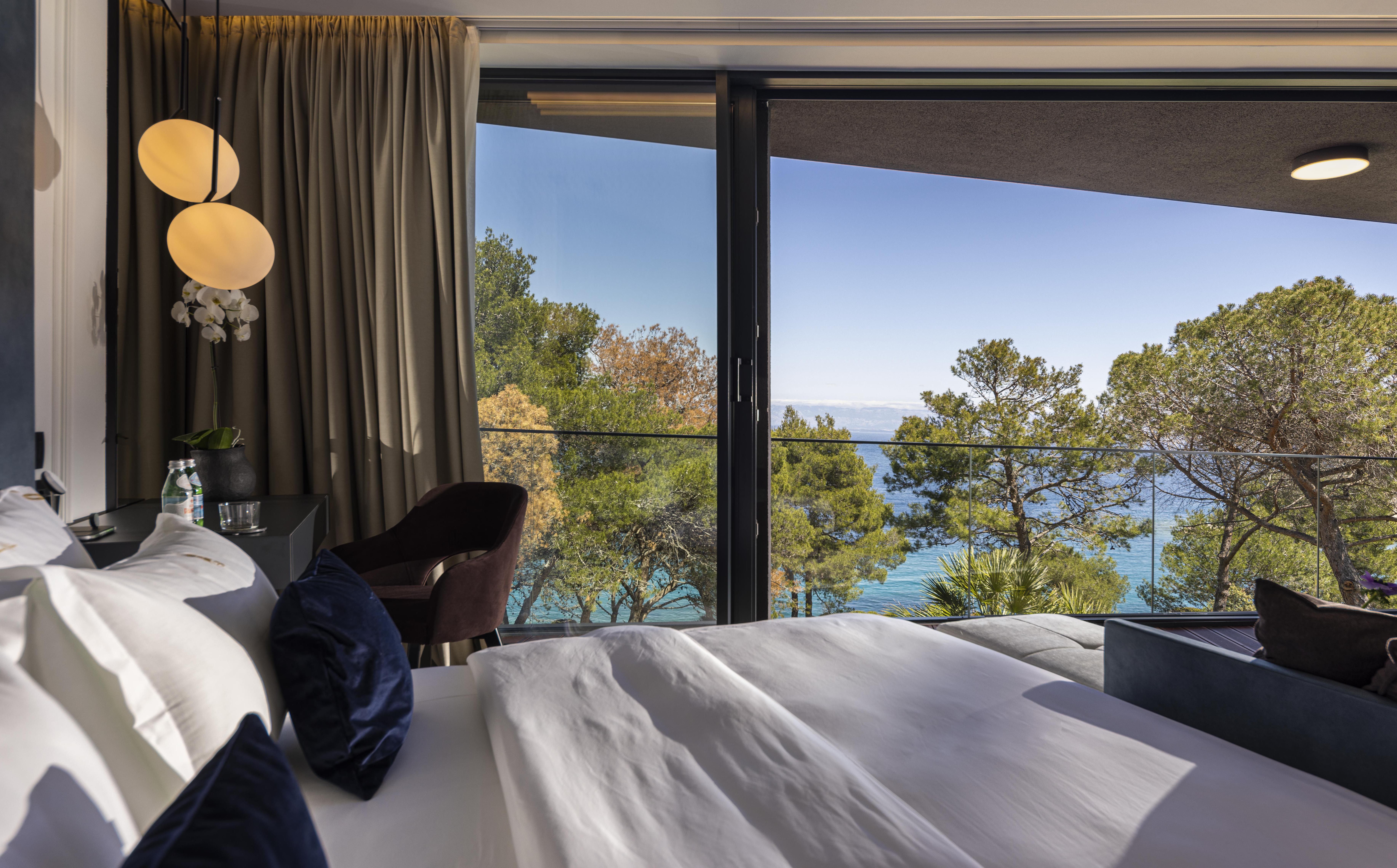 Modern bedroom with a bed and a panoramic view of the sea and trees through large glass windows in Villa Duchess in Mali Losinj