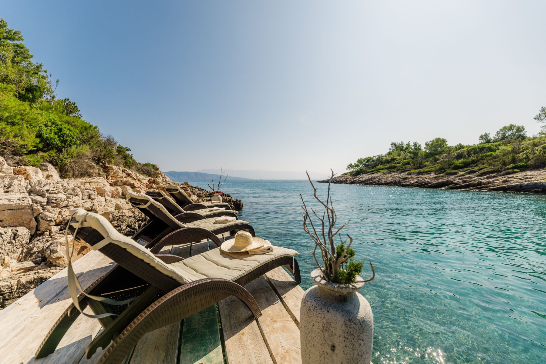 A wooden dock at Villa Hidden Retreat in Jelsa, featuring lounge chairs and a vase, set in a tranquil bay.
