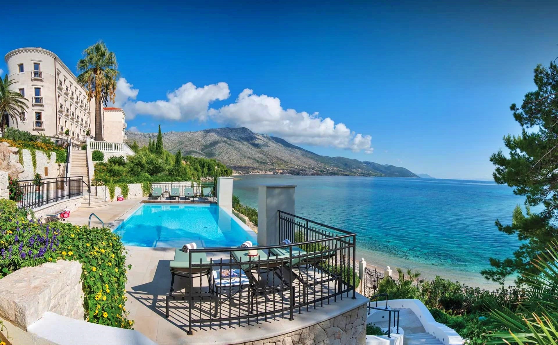 A scenic coastal view of Villa Korta Katarina with a swimming pool, mountains, and a clear blue sky