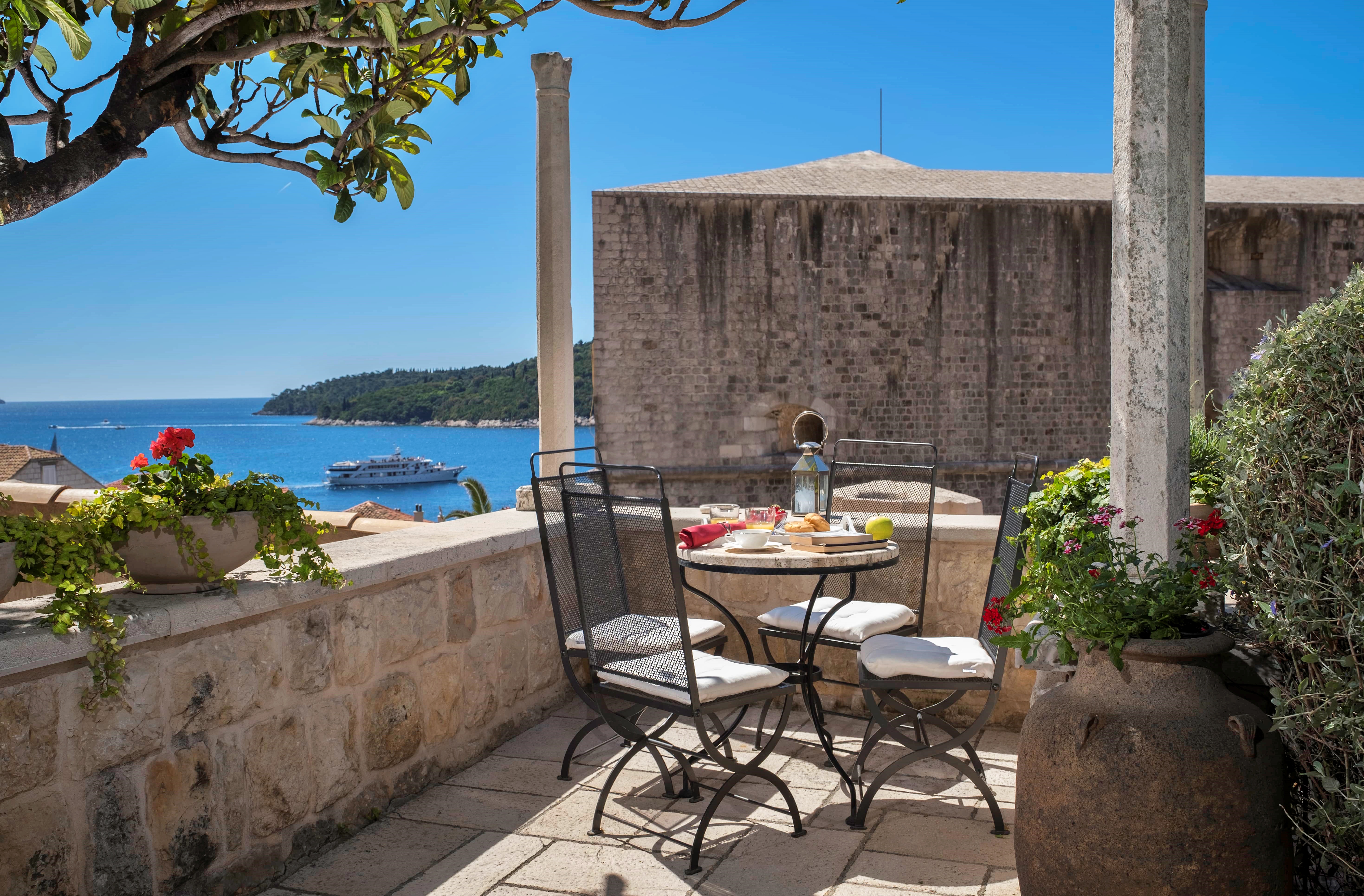 Outdoor dining area in Villa Vita Dubrovnik with a table set for breakfast overlooking the sea and stone buildings.