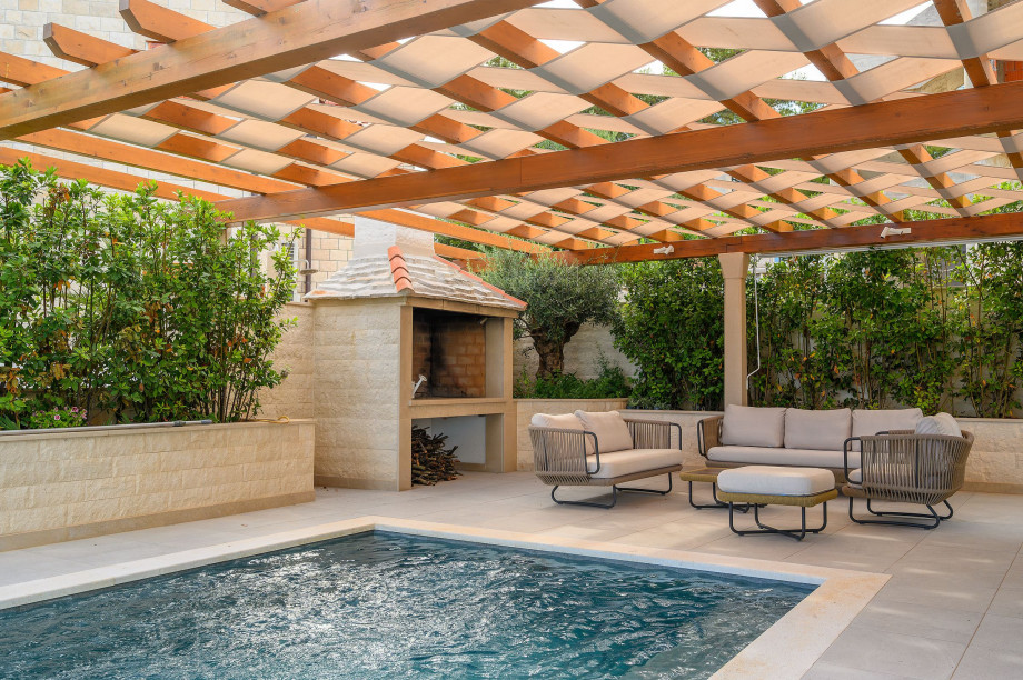 An inviting pool in Villa Blanc Brac surrounded by a pergola and elegant outdoor furniture, perfect for enjoying sunny days.