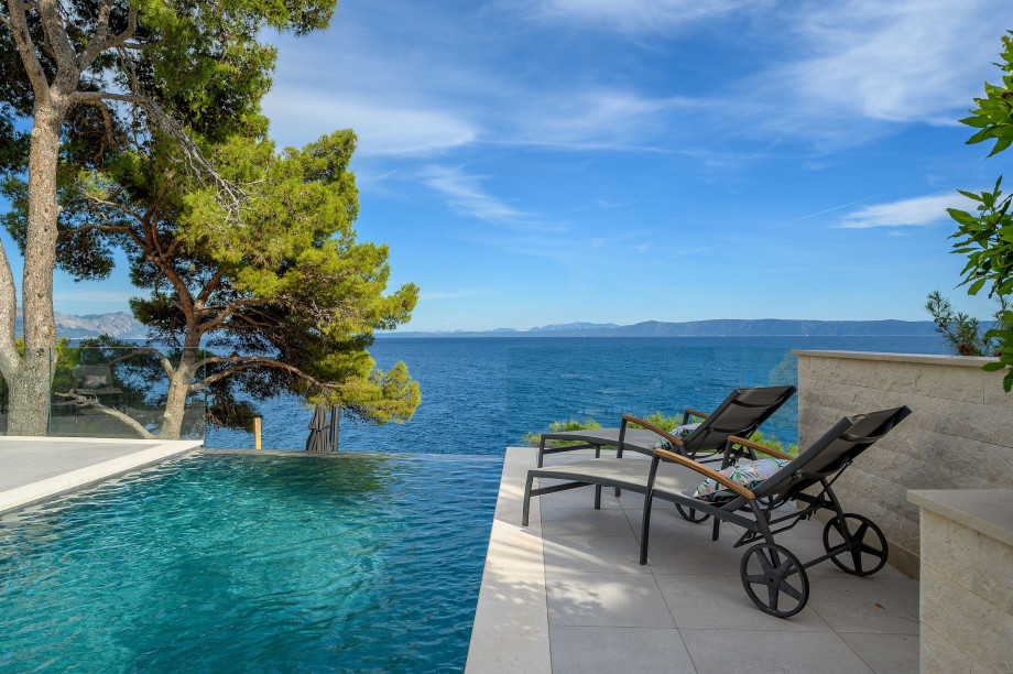 A picturesque pool of Villa Blanc Brac surrounded by chairs, offering a breathtaking view of the Adriatic Sea